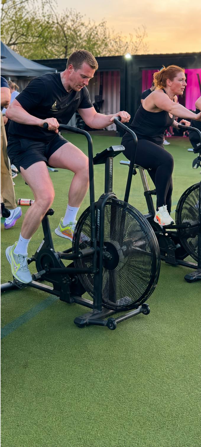 Members on air bikes during an outdoor BODY HEALTH FITNESS session at sunset